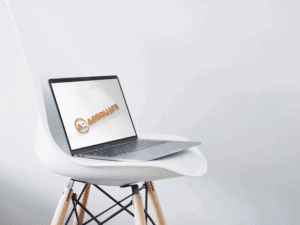 A laptop displaying a logo with text "Adequate" and a circular design is placed on a modern, white, molded plastic chair with wooden legs. The chair and laptop are set against a minimalist white background.