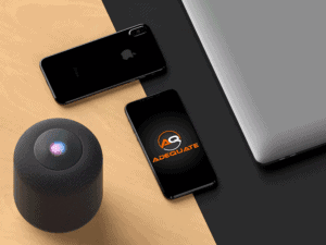 A sleek workspace setup featuring a black smart speaker, two smartphones (one displaying an "Adequate" logo), and part of a laptop on a wooden and black surface. The smart speaker has a colorful light on top. All devices are arranged neatly.