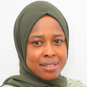 A woman wearing a green hijab smiles softly. She has a nose ring and is against a plain white background.