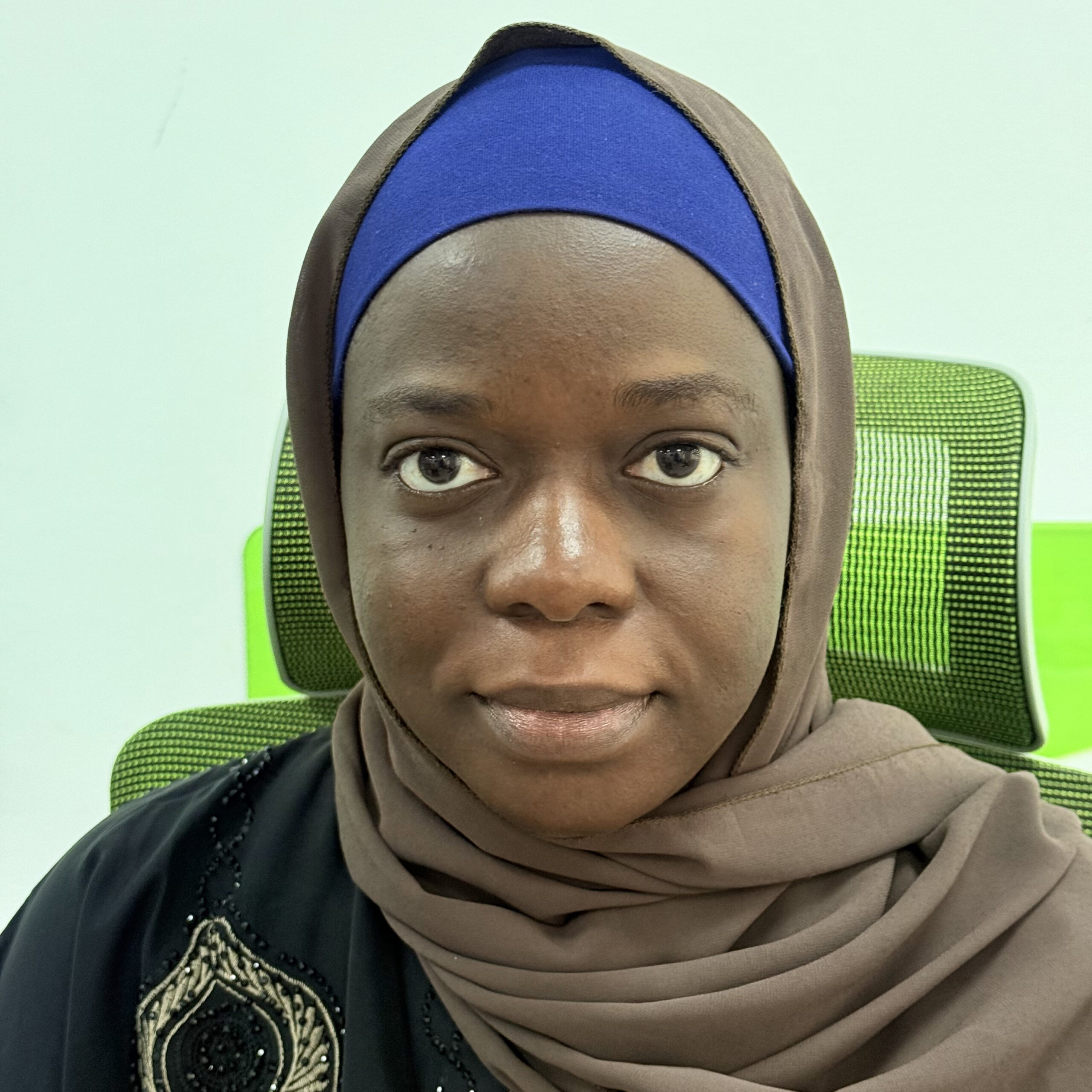 Binta Khan Badjie A stylized graphic of a green tree with four horizontal layers of leaves and a brown trunk, resembling a palm tree. The trunk is centrally aligned, and there is a green crescent shape at the bottom. A small green crescent sits at the top of the tree.